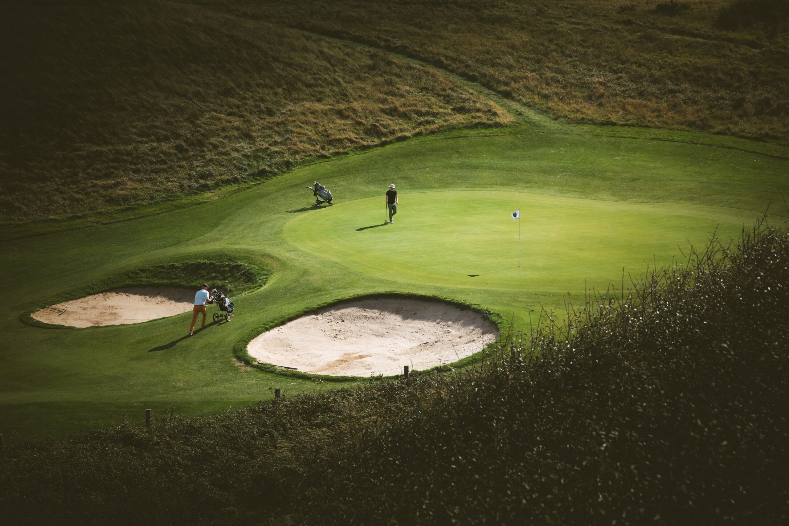 Golfers on a sunlit links green with bunkers in Ireland